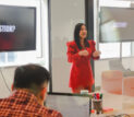 A facilitator leads an executive training session for DBS Bank executives in a modern meeting room, presenting to participants seated around a conference table while presentation screens display the word “QUESTION?”.