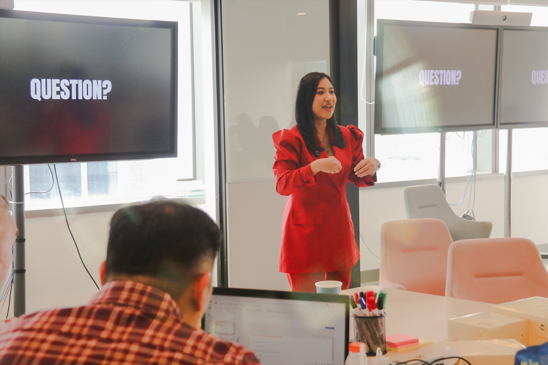 A facilitator leads an executive training session for DBS Bank executives in a modern meeting room, presenting to participants seated around a conference table while presentation screens display the word “QUESTION?”.