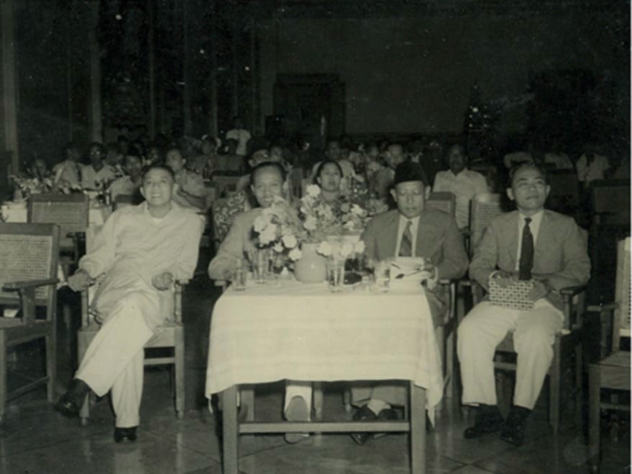 Black-and-white photograph of four officials seated at a table during a formal gathering, with an audience behind them. According to the accompanying caption, the event is an introductory evening for Information Service officials attended by Sri Paku Alam VIII and Information Minister Wiwoho Poerbohadidjojo in Yogyakarta on 6 November 1950.